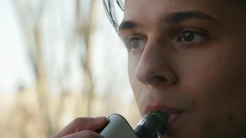 Handsome boy smoking e-cigarette outdoors. Face of vaping person in slow motion Vidéo 105754269