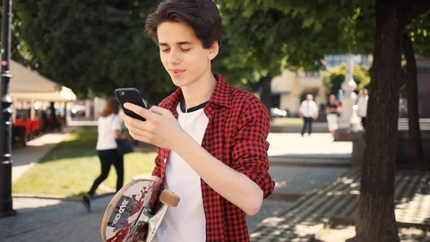 Handsome boy using a mobile phone smile walk keeps skate guy business fashion Stock Footage 92051050