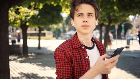 Handsome boy using mobile phone listens to music in headphones walk keeps skate Stock Footage 92051074