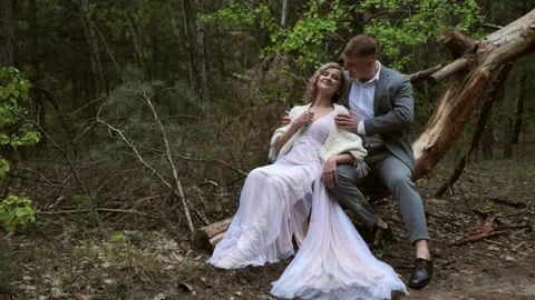 Handsome bride and groom sit cutely on a log in the forest Stock Footage 274162600