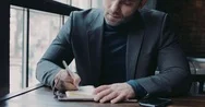 Handsome Businessman In A Formal Outfit Sits In The Café And Signs Papers  Stock Footage
