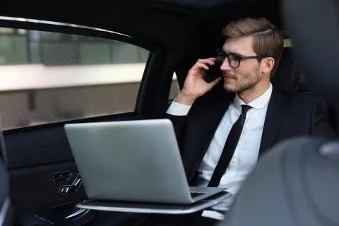 Handsome businessman talking on smartphone, using laptop while sitting in car. Stock Photos