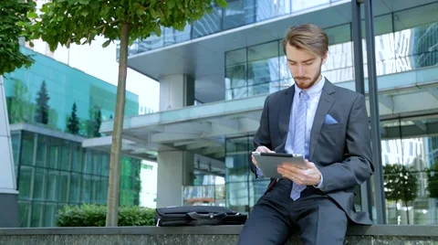 Handsome businessman is using tablet computer near the modern business center Stock Footage 67583256