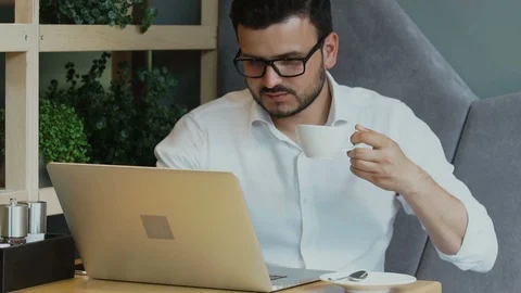 Handsome businessman working on his computer and drinking from white cup in cafe Stock Footage 112989230