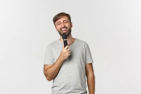 Handsome carefree guy singing song in karaoke, holding microphone, standing over Stock Photos
