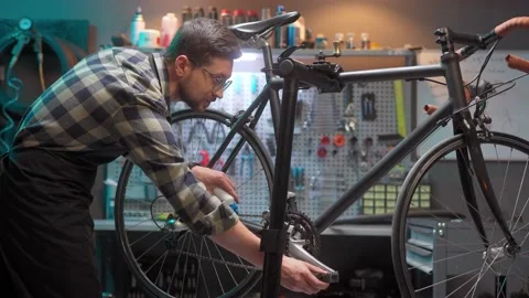 Handsome caring skillful man repairing and maintaining bicycle in modern Stock Footage 232489616
