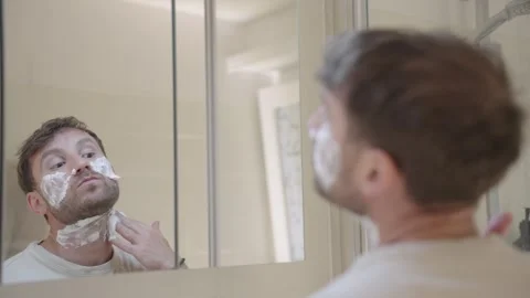 Handsome caucasian man applying shaving cream to his face and neck while looking Stock Footage 335204545