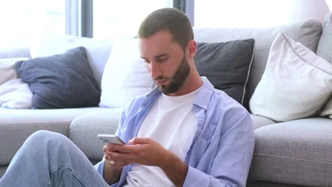Handsome caucasian man with a beard sitting on the floor in his living room Vídeos de archivo 344781142
