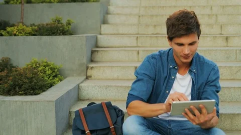 Handsome caucasian man sitting on the steps outdoors and using tablet device. Stock Footage 80797648