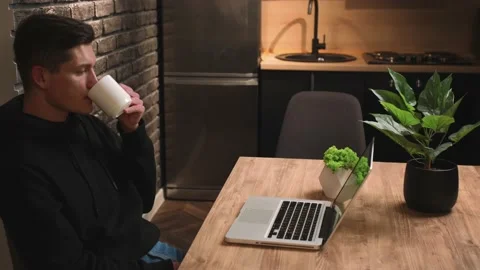 Handsome caucasian Man using laptop, looking at laptop screen. Man drinking Stock Footage 148384239
