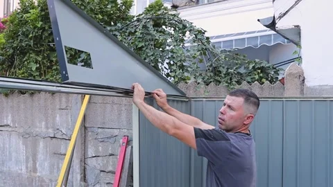 A handsome Caucasian worker installs a triangular piece on a profile shed. Stock Footage 322553982