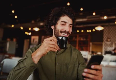 Handsome cheerful caucasian man using mobile phone while drinking coffee in Stock Photos