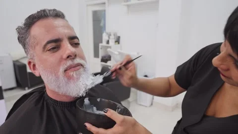 Handsome client showing satisfaction during beard dyeing in beauty salon 스톡 동영상 255795873