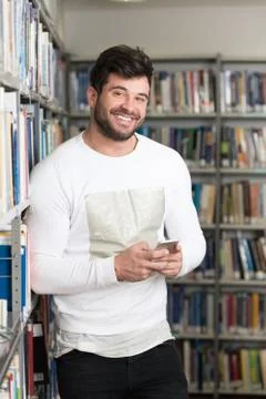 Handsome College Student Using Mobile Phone In Library Stock Photos