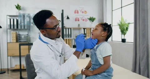 Handsome confident professional black-skinned male doctor examining small girl's Stock Footage 156259285