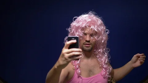 Handsome crazy guy with a beard and in a pink wig makes sephi from a smartphone Stock Footage 117071114