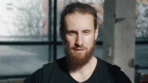 A handsome curly-haired guy with a beard looks at the camera.  Stock Footage 168373838