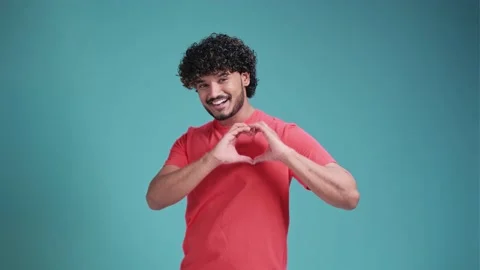 Handsome curly millennial hindu guy wearing coral t-shirt showing heart-shaped Stock Footage 238516802