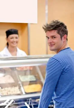 Handsome customer standing in the queue in a cafeteria smiling at the camera Stock Photos