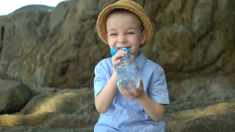 Handsome cute boy drinks clear water from a plastic bottle on a sunny day. Stock Footage 106205572
