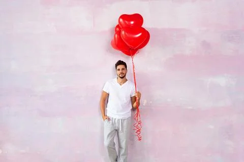 Handsome cute young man posing on the pink wall with red heart shaped balloon Stock-Fotos
