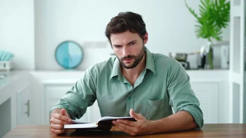 Handsome dark-haired young Caucasian man relaxing at home, leafing through the Stock Footage 212420487