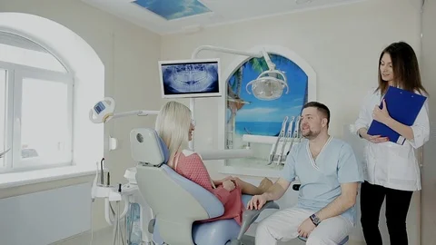 Handsome dentist with his assistant talking with female patient as to her Stock Footage 104353236