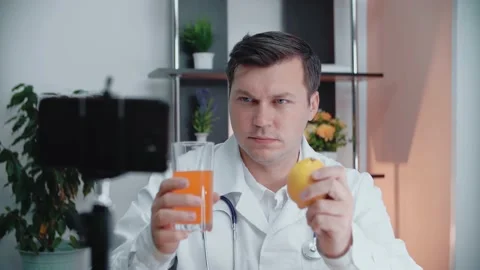 Handsome doctor talking to the camera, holding a glass with juice and lemon Stock Footage 154254045