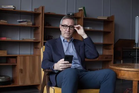 Handsome elderly grey haired man in glasses looking on his mobile phone, si.. Stockfoto's