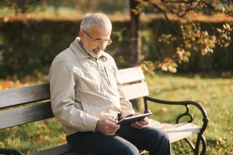 Handsome elderly man sitting on the bench and use tablet for scrolling in 写真素材