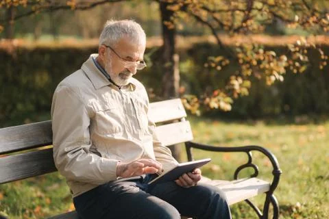 Handsome elderly man sitting on the bench and use tablet for scrolling in Stock Photos
