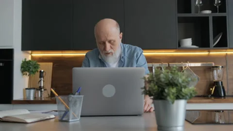 Handsome elderly man, working at laptop and talking via video chat zoom, sitting Stock Footage 156352751