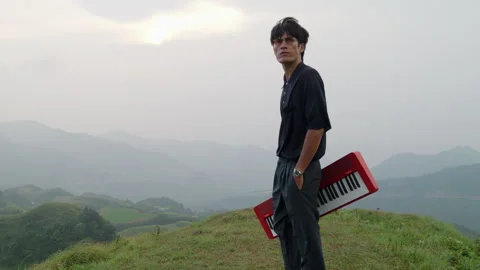 Handsome elegant asian man walking on hilltop holding an electronic piano. Stock Footage 247443347