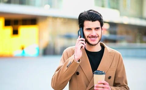 Handsome elegant dressed man talking on the phone and holding a cup of coffee Stock Photos