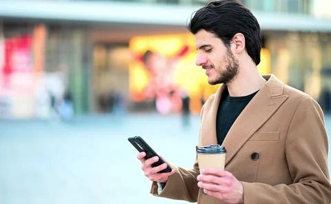 Handsome elegant dressed man using his smartphone and holding a cup of coffee Stockfoto's