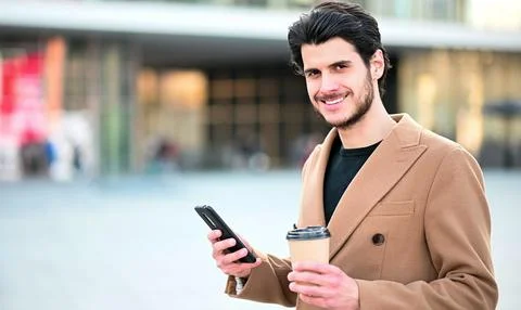 Handsome elegant dressed man using his smartphone and holding a cup of coffee Stock Photos