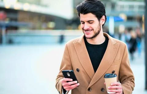 Handsome elegant dressed man using his smartphone and holding a cup of coffee Stock Photos