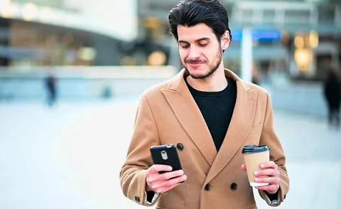 Handsome elegant dressed man using his smartphone and holding a cup of coffee Stock Photos