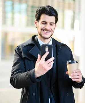 Handsome elegant dressed man using his smartphone and holding a cup of coffee Stock Photos