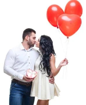 Handsome elegant guy is presenting a heart shaped gift and balloons to his Stock Photos