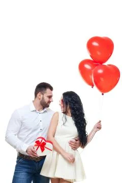 Handsome elegant guy is presenting a heart shaped gift and balloons to his Stock Photos