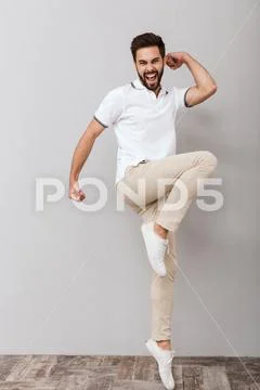 Handsome emotional man make winner gesture indoors isolated over grey backgro Stock Photos