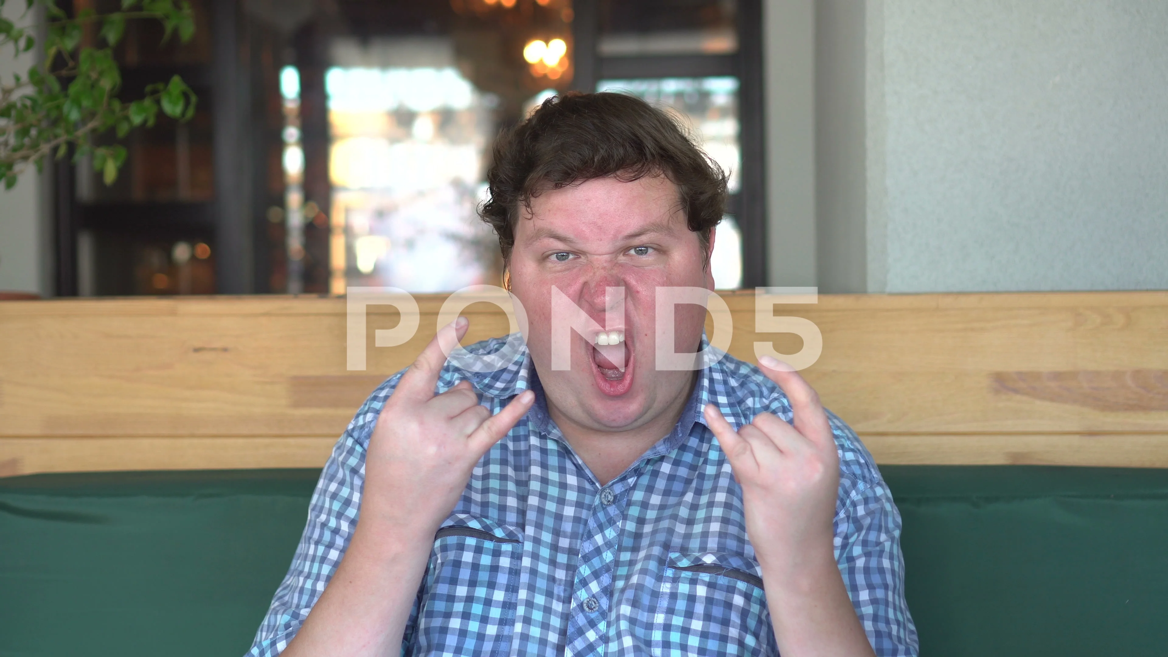 A handsome, fat man with big body shows sign of the horns in the cafe or