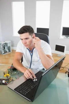 Handsome focused computer engineer examining laptop with stethoscope Stock Photos