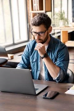 Handsome focused man working using laptop sitting at office desk table Stock Photos