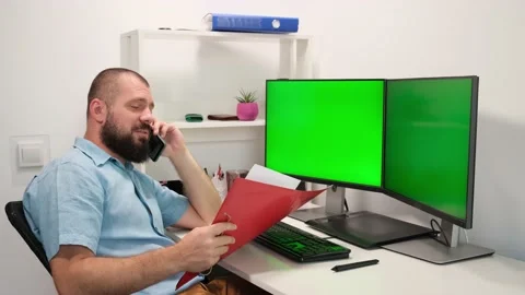 Handsome freelancer man looking at folder, sitting against Two monitors with Stock Footage 139136088