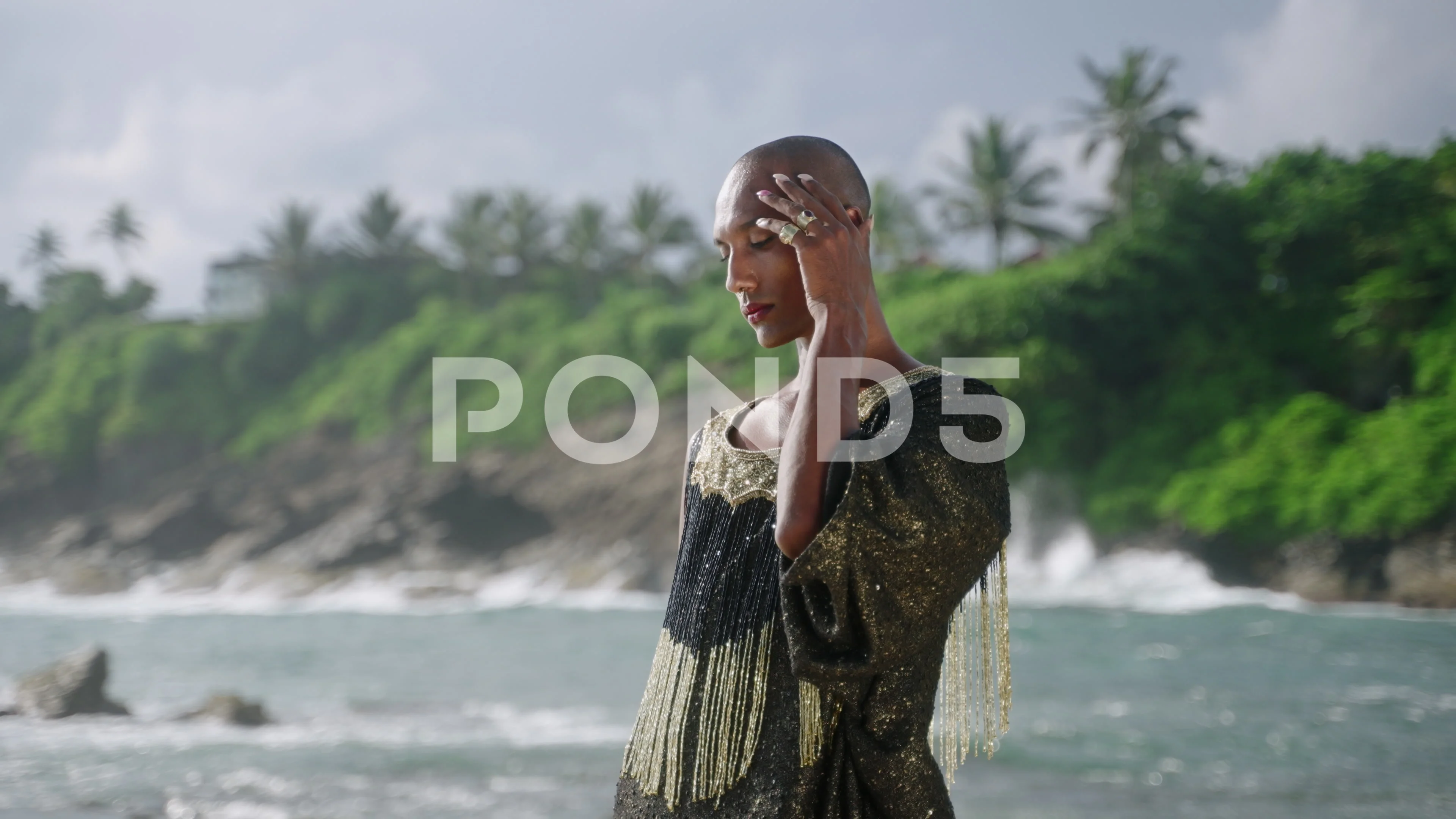 Handsome gay black man in luxury gown poses on scenic ocean beach. Gender  fluid