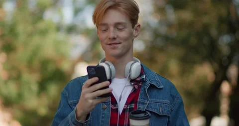 Handsome Ginger Guy walking at Park while Browsing Modern Smartphone. Caucasian Stock Footage 163223345