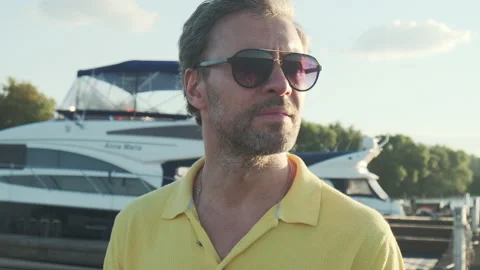 Handsome good-looking mature man wearing sunglasses, yacht pier in marina at Stockbeeldmateriaal 143545643