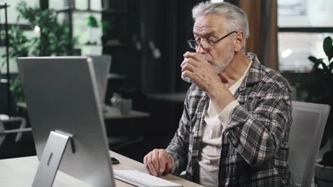 Handsome gray haired businessman drinking clean water from glass while working Stock Footage 253513610